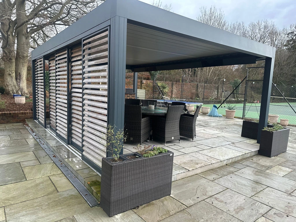 A grey cube-shaped pergola covering an outdoor seating and dining area