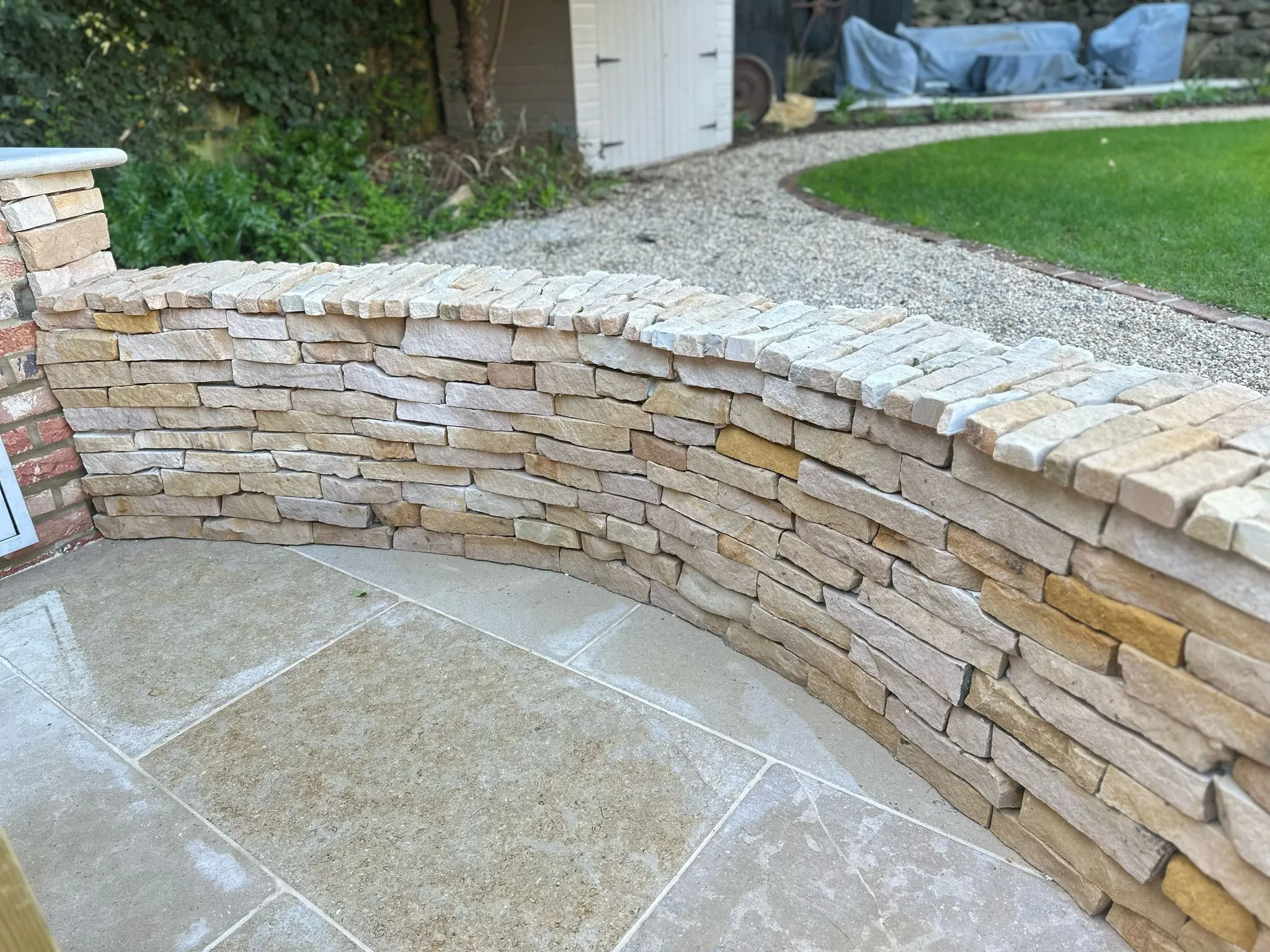 A small brick wall along the perimeter of a paved outdoor entertainment area, with some of the rest of the garden visible in the background